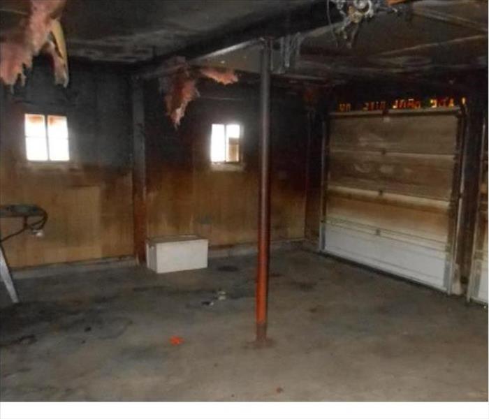 garage fire left sooty deposits on the walls and garage door and the floor. Some hanging insulation is visible.