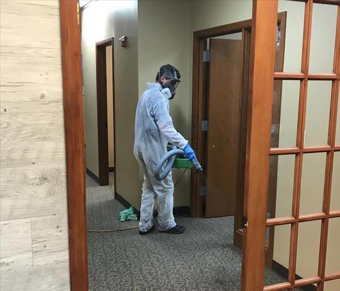 Employee in full PPE sanitizing commercial building
